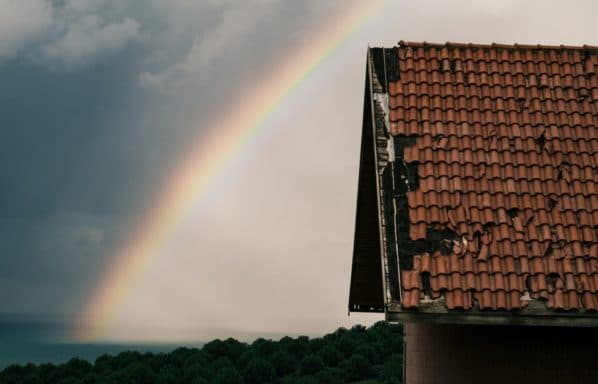 Can you sell a house with a bad roof? A bad shingle roof with a rainbow behind it.
