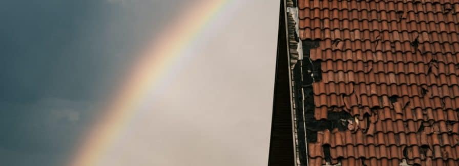 Can you sell a house with a bad roof? A bad shingle roof with a rainbow behind it.