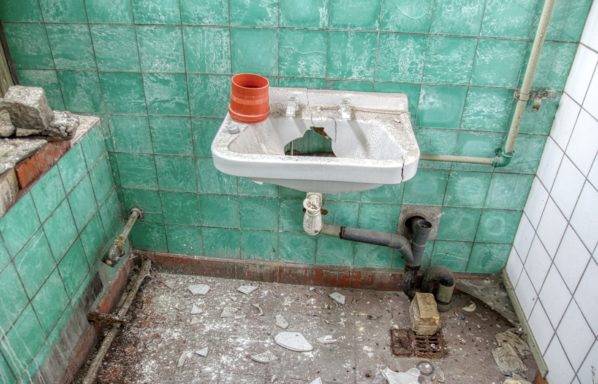 Damaged green tiles and plumbing showing How to sell your house with bad plumbing