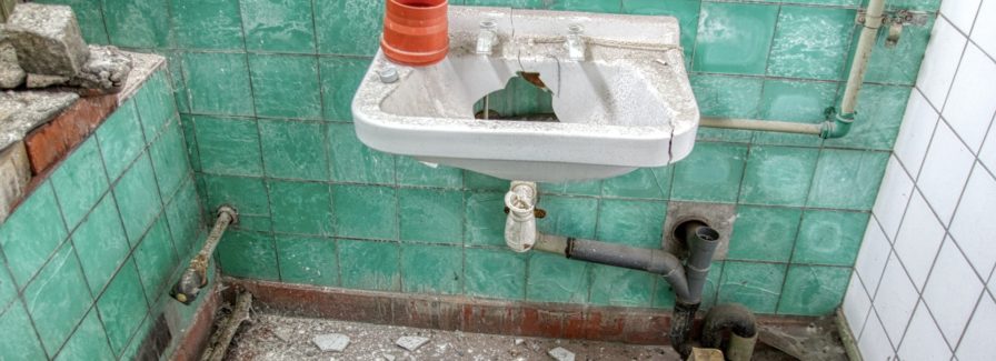 Damaged green tiles and plumbing showing How to sell your house with bad plumbing