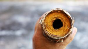 A man holds a galvanized steel pipe showing rust and blockage.