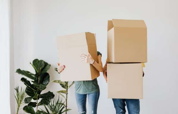 Can You sell a rental property with bad tenants? Two adults hold moving boxes in a white room of a rental home.